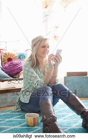 Stock Photograph - Mature woman sitting on floor texting on cellphone. Fotosearch