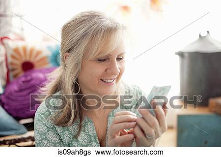 Mature woman texting on cellphone in living room View Large Photo Image Stock Photograph - Mature woman texting on cellphone in living room. Fotosearch