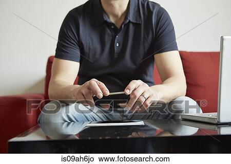 Mid adult man holding smartphone with digital tablet and laptop on table View Large Photo Image Picture - Mid adult man holding smartphone with digital tablet and laptop on table. Fotosearch