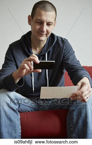 Mid adult man sitting on sofa photographing paper with smartphone View Large Photo Image Stock Image - Mid adult man sitting on sofa photographing paper with smartphone. Fotosearch