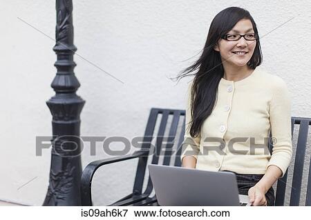 Stock Photo - Mid adult woman sitting on bench with laptop. Fotosearch
