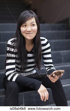 Mid adult woman sitting on steps holding smartphone View Large Photo Image Stock Photograph - Mid adult woman sitting on steps holding smartphone. Fotosearch