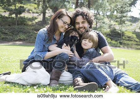 Stock Photograph - Portrait of family with two boys and dog sitting in park. Fotosearch