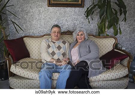Stock Image - Portrait of mature couple sitting on ornate sofa. Fotosearch