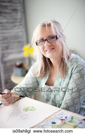 Stock Image - Portrait of mature female artist watercolour painting in studio. Fotosearch