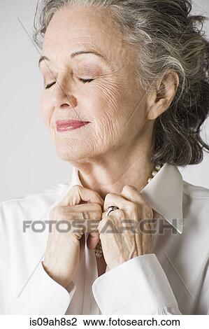 Stock Image - Portrait of senior woman, hands on collar, eyes closed. Fotosearch