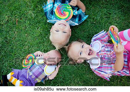 Stock Photograph - Siblings with lollipops lying on grass. Fotosearch