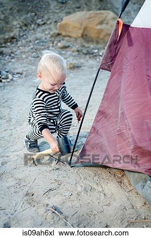 Stock Image - Toddler hammering tent peg with mallet. Fotosearch