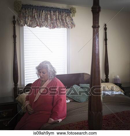 Picture - Unhappy mature woman sitting on bed. Fotosearch
