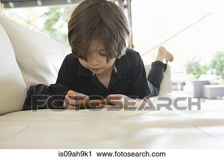 Young boy lying on sofa playing on hand held video game View Large Photo Image Stock Image - Young boy lying on sofa playing on hand held video game. Fotosearch
