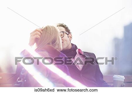 Stock Image - Young couple kissing on park bench, New York, USA. Fotosearch