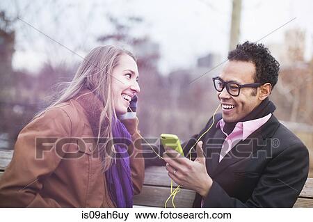 Young couple listening to music from smartphone in park View Large Photo Image Stock Photo - Young couple listening to music from smartphone in park. Fotosearch