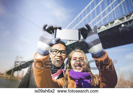 Stock Image - Young couple photographing themselves with Brooklyn Bridge, New York, USA. Fotosearch