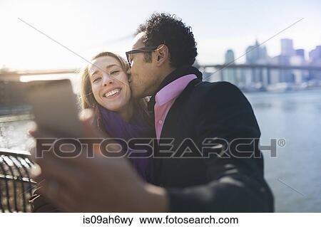 Stock Photo - Young couple taking selfie and kissing, New York, USA. Fotosearch