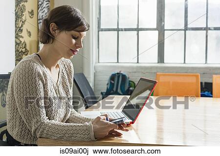 Stock Image - Young female designer texting on smartphone in design studio. Fotosearch