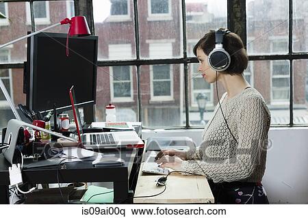 Stock Photography - Young female designer wearing headphones in design studio. Fotosearch