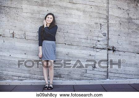 Stock Photo - Young woman standing, leaning against wall. Fotosearch