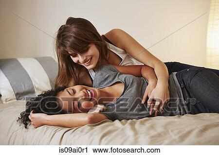 Stock Image - Affectionate young female couple relaxing on bed. Fotosearch