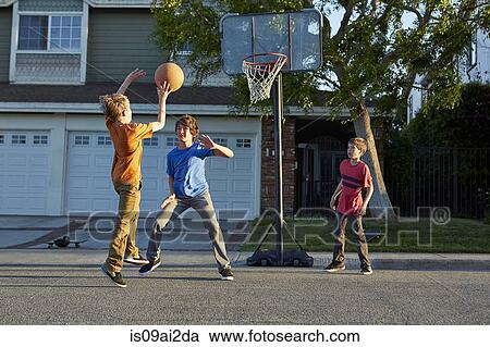 Stock Image - Boys playing basketball outside house. Fotosearch