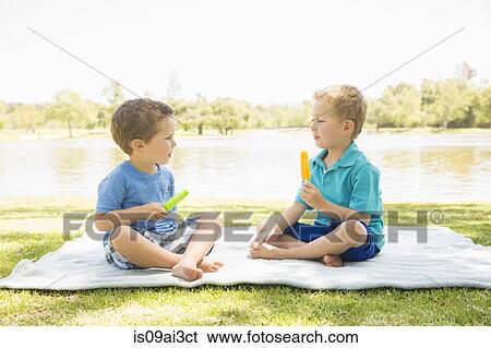 Stock Photograph - Brothers on picnic blanket holding ice lolly, Newport Beach, California, USA. Fotosearch