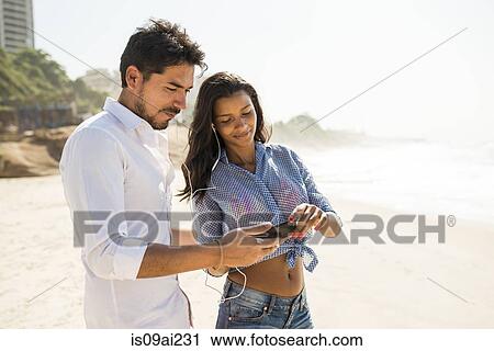 Couple choosing music from smartphone, Arpoador beach, Rio De Janeiro, Brazil View Large Photo Image Stock Image - Couple choosing music from smartphone, Arpoador beach, Rio De Janeiro, Brazil. Fotosearch