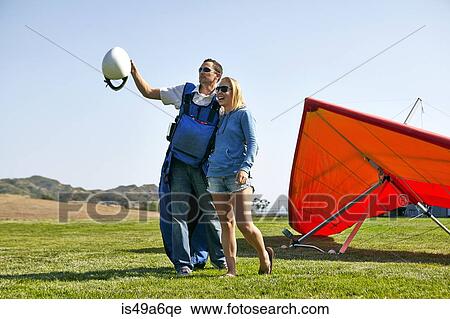Stock Image - Couple enjoying view, hang glider in background. Fotosearch