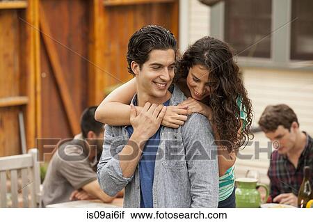 Stock Image - Couple in garden, with arm around, friends in background. Fotosearch