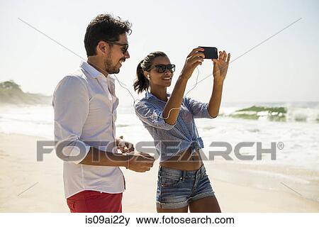 Stock Photo - Couple sharing music from smartphone, Arpoador beach, Rio De Janeiro, Brazil. Fotosearch