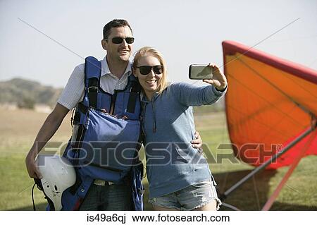 Stock Image - Couple taking selfie, hang glider in background. Fotosearch