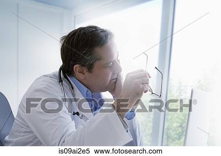 Stock Photography - Doctor holding eyeglasses, rubbing eyes. Fotosearch