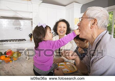 Female toddler feeding snack to grandfather in kitchen View Large Photo Image Stock Image - Female toddler feeding snack to grandfather in kitchen. Fotosearch