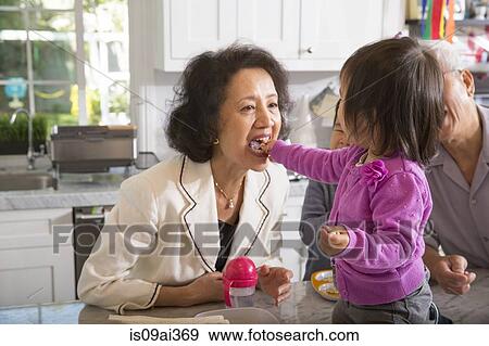 Female toddler feeding snack to grandmother in kitchen View Large Photo Image Stock Photo - Female toddler feeding snack to grandmother in kitchen. Fotosearch