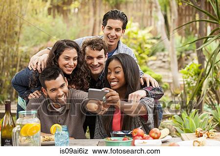 Stock Photo - Friends at barbecue, taking self portrait photograph using smartphone. Fotosearch
