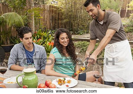 Stock Photograph - Friends sitting around table sharing barbecue food. Fotosearch