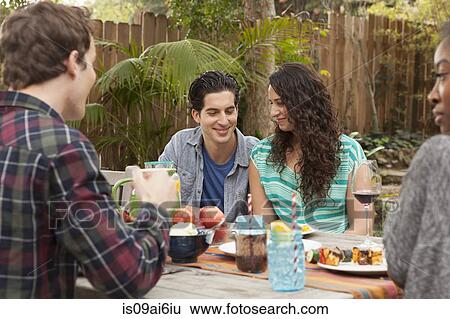 Friends sitting around table sharing barbecue food View Large Photo Image Stock Photograph - Friends sitting around table sharing barbecue food. Fotosearch