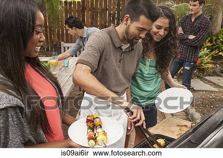 Friends sitting around table sharing barbecue food View Large Photo Image Stock Photography - Friends sitting around table sharing barbecue food. Fotosearch