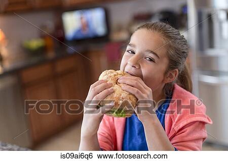 Stock Photograph - Girl in kitchen biting sandwich. Fotosearch