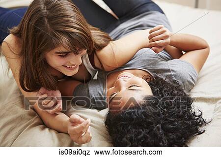 Happy young female couple reclining on bed View Large Photo Image Stock Photo - Happy young female couple reclining on bed. Fotosearch