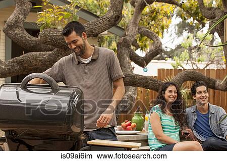 Man cooking on barbecue, friends in background View Large Photo Image Picture - Man cooking on barbecue, friends in background. Fotosearch