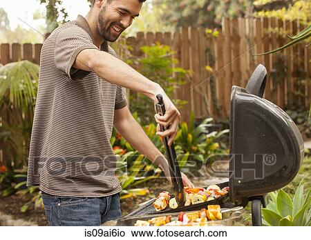 Picture - Man cooking vegetable skewers on barbecue. Fotosearch