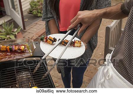 Stock Photography - Man cooking vegetable skewers on barbecue. Fotosearch