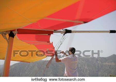 Stock Image - Man repairing hang glider. Fotosearch