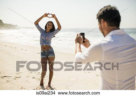 Mid adult man photographing girlfriend on smartphone, Arpoador beach, Rio De Janeiro, Brazil View Large Photo Image Picture - Mid adult man photographing girlfriend on smartphone, Arpoador beach, Rio De Janeiro, Brazil. Fotosearch
