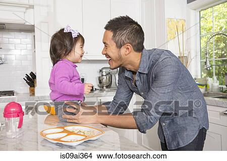 Picture - Mid adult man with toddler daughter on kitchen counter. Fotosearch