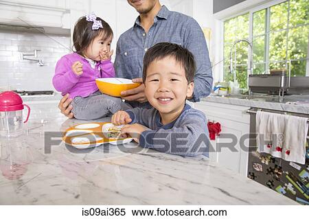 Stock Photography - Mid adult man with two young children snacking in kitchen. Fotosearch