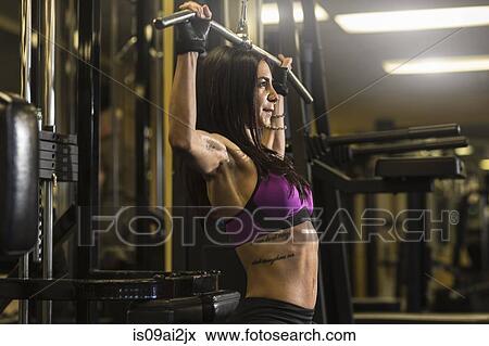 Stock Photo - Mid adult woman in gym doing pectoral exercise. Fotosearch