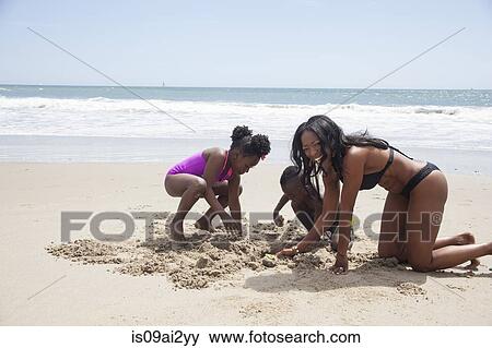 Stock Photo - Mother and children digging in sand on beach. Fotosearch