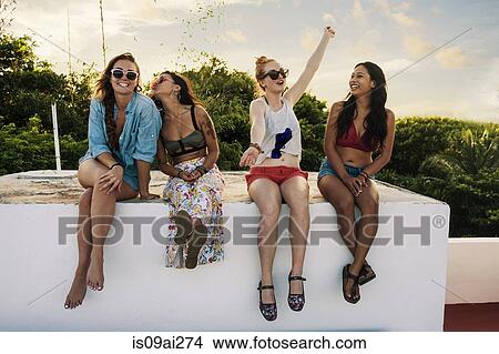 Picture - Portrait of four young female friends sitting on wall. Fotosearch