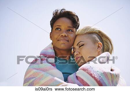 Stock Photograph - Portrait of lesbian couple wrapped in a blanket. Fotosearch
