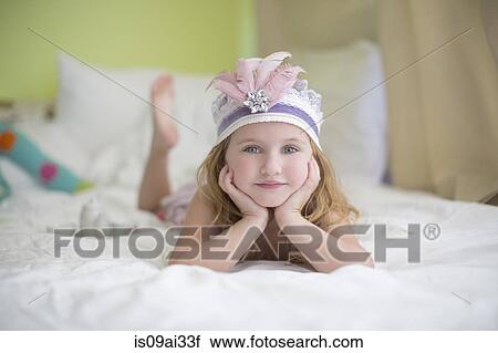 Stock Image - Portrait of young girl in princess headdress on bed. Fotosearch
